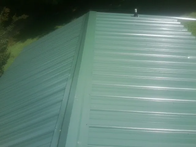 New green metal panels meeting at the ridge of a roof — Flat Roof Repair work by our crew in Hamilton
